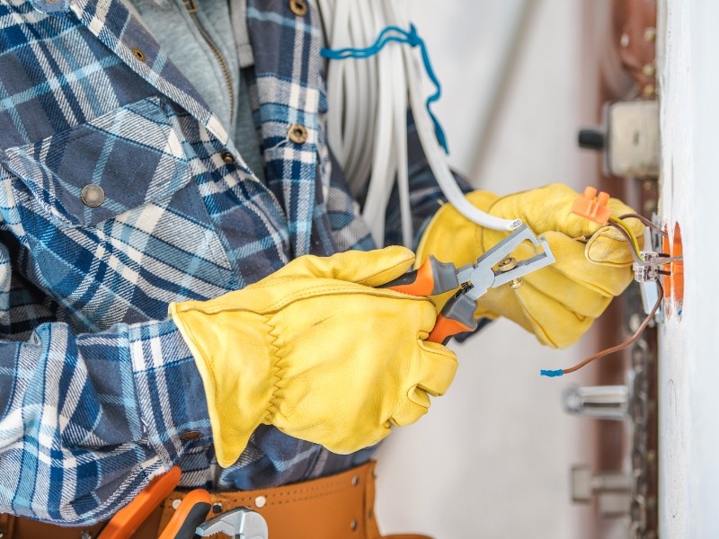 An electrician wearing safety gear and gloves uses pliers to tweak an electrical wire